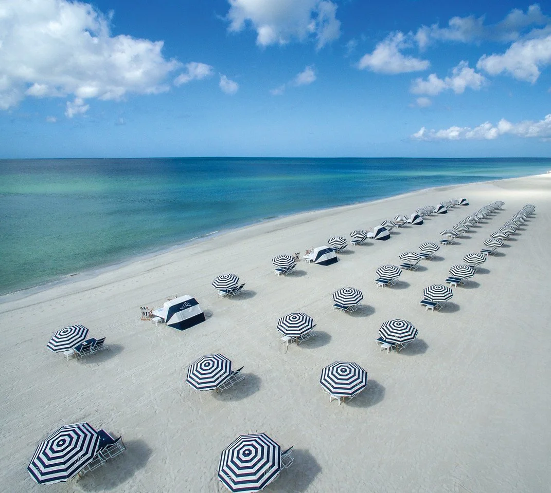 Aerial view of the private beach at The Resort at Longboat Key Club with rows of blue and white umbrellas and loungers
