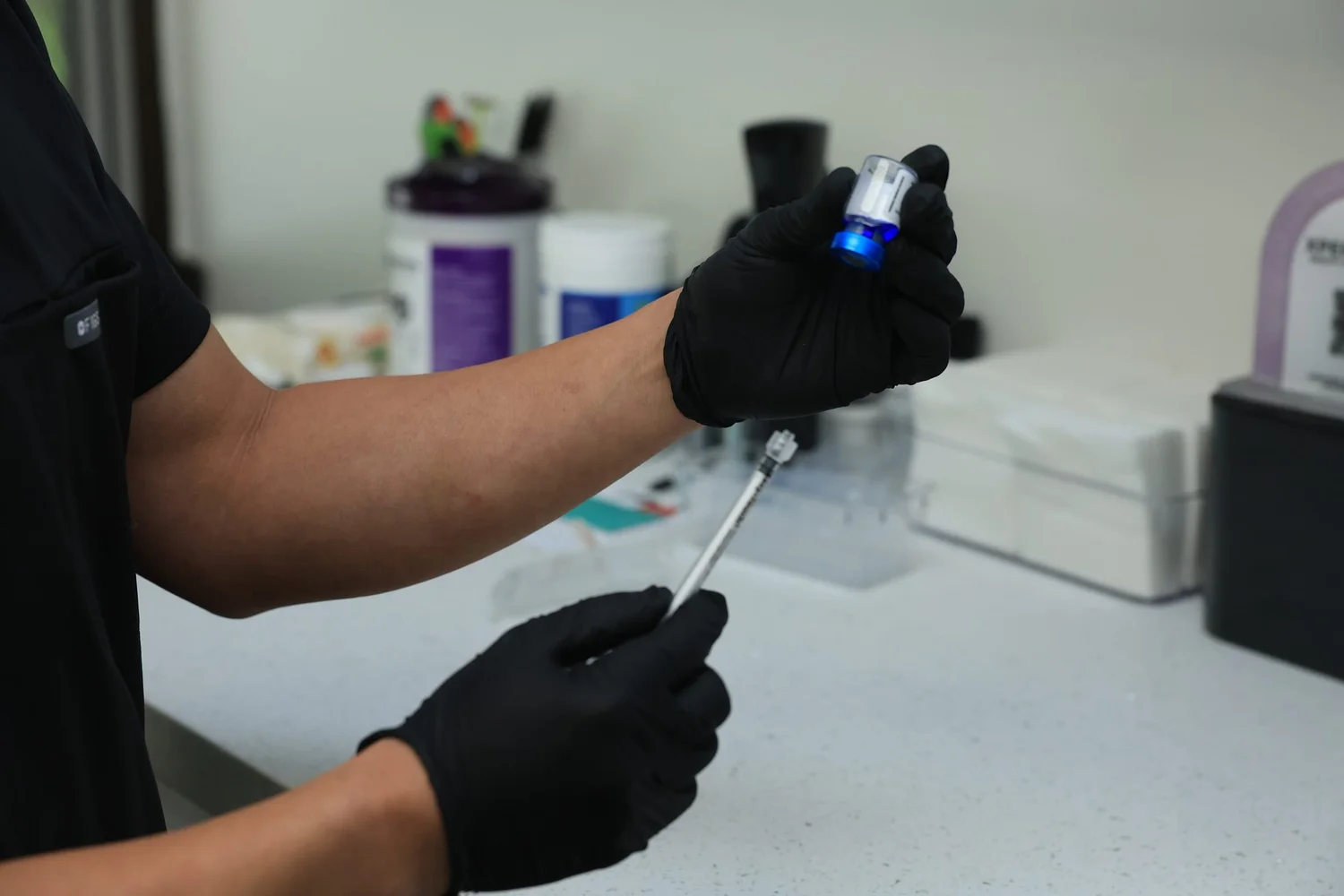Gloved clinician preparing an injectable at a counter