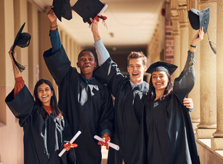 Four graduates celebrate together in graduation gowns.