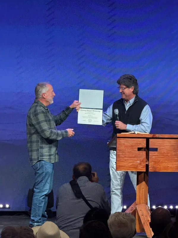 David Guzik stands beside a displayed honorary doctorate certificate during an award presentation.