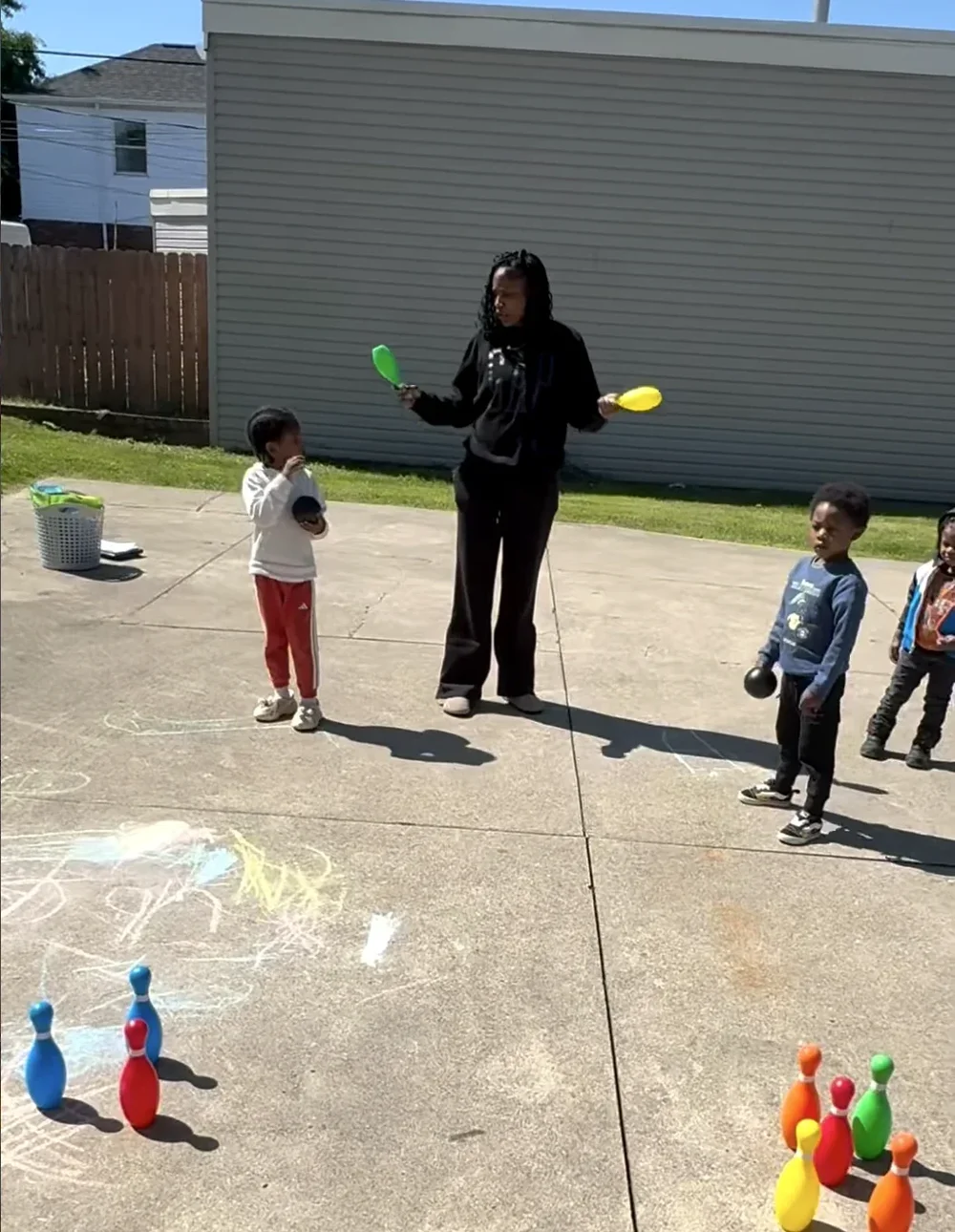 A teacher leading a game of outdoor bowling with preschoolers