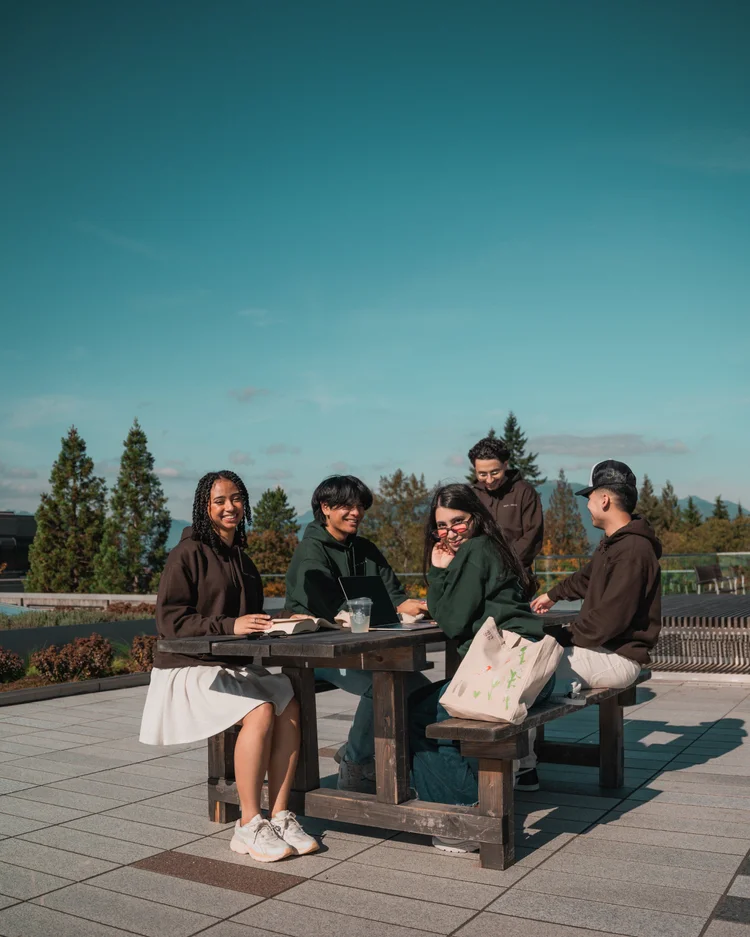 Students sitting together outdoors among the trees.