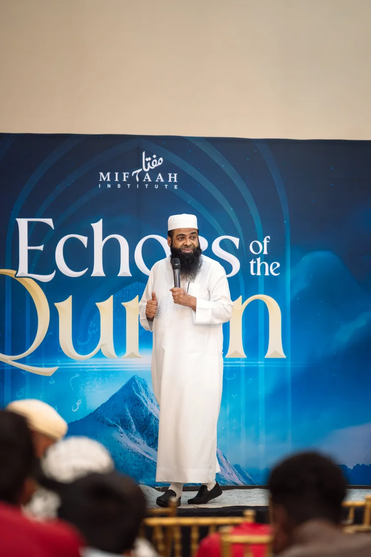 A speaker on stage in front of the Echoes of the Quran backdrop.