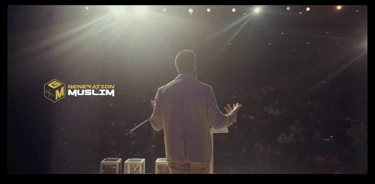 A speaker on a dark stage facing the audience at an NYM INK event.
