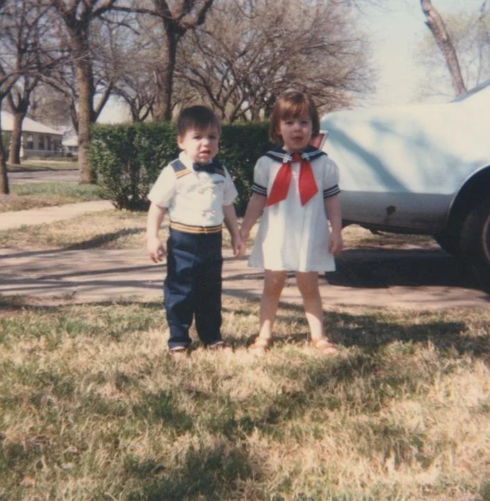 Two little kids holding hands on a front lawn