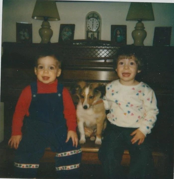 Two kids in matching sweaters sitting with a collie