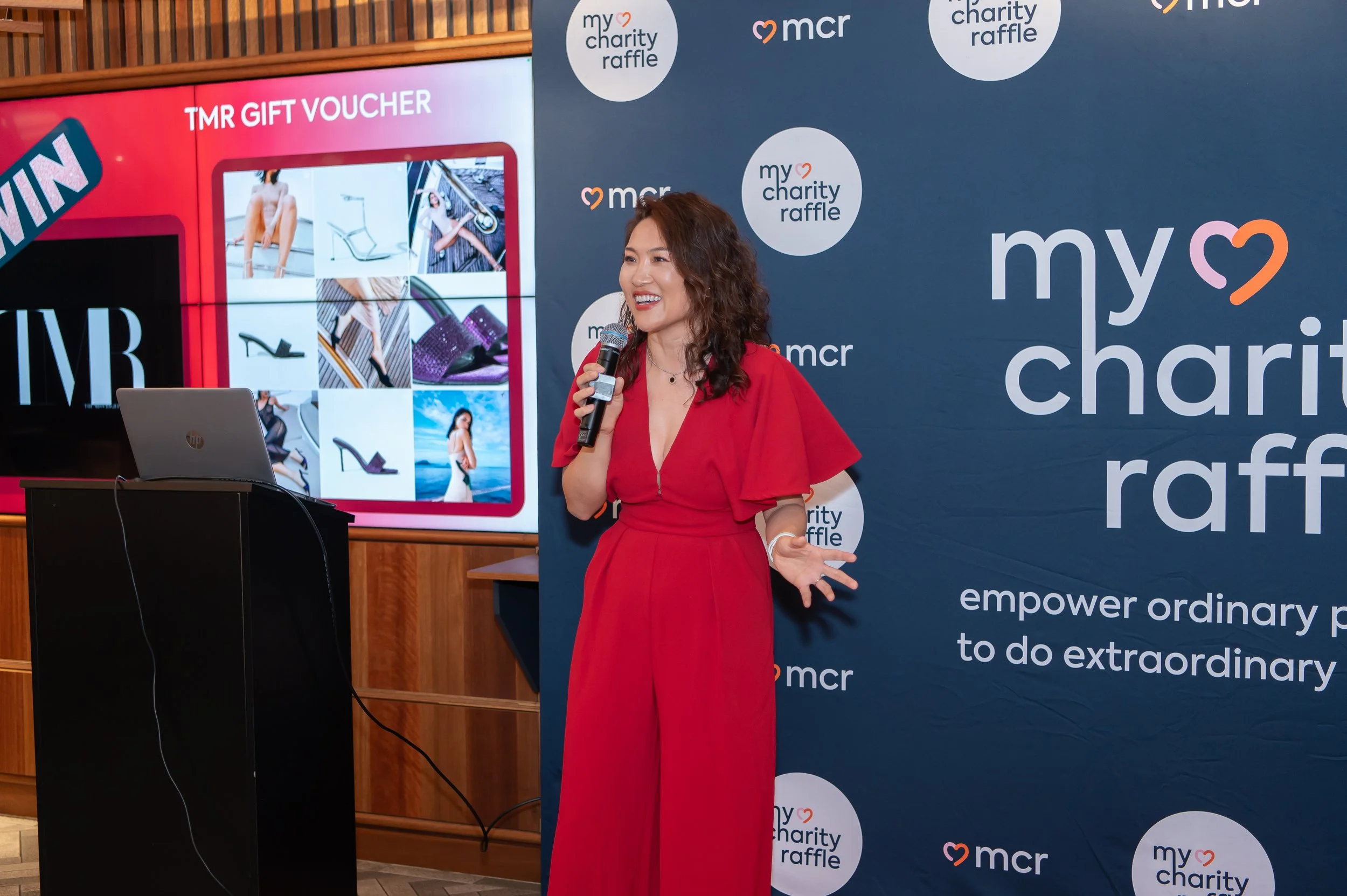 The My Charity Raffle host speaking at a raffle event, in front of the My Charity Raffle backdrop