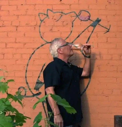 Chef Claud Beltran sipping wine in front of the Bacchus pig mural in Pasadena