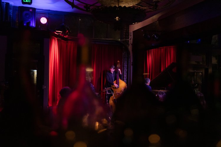 A bassist playing in front of the red curtains at Bacchus