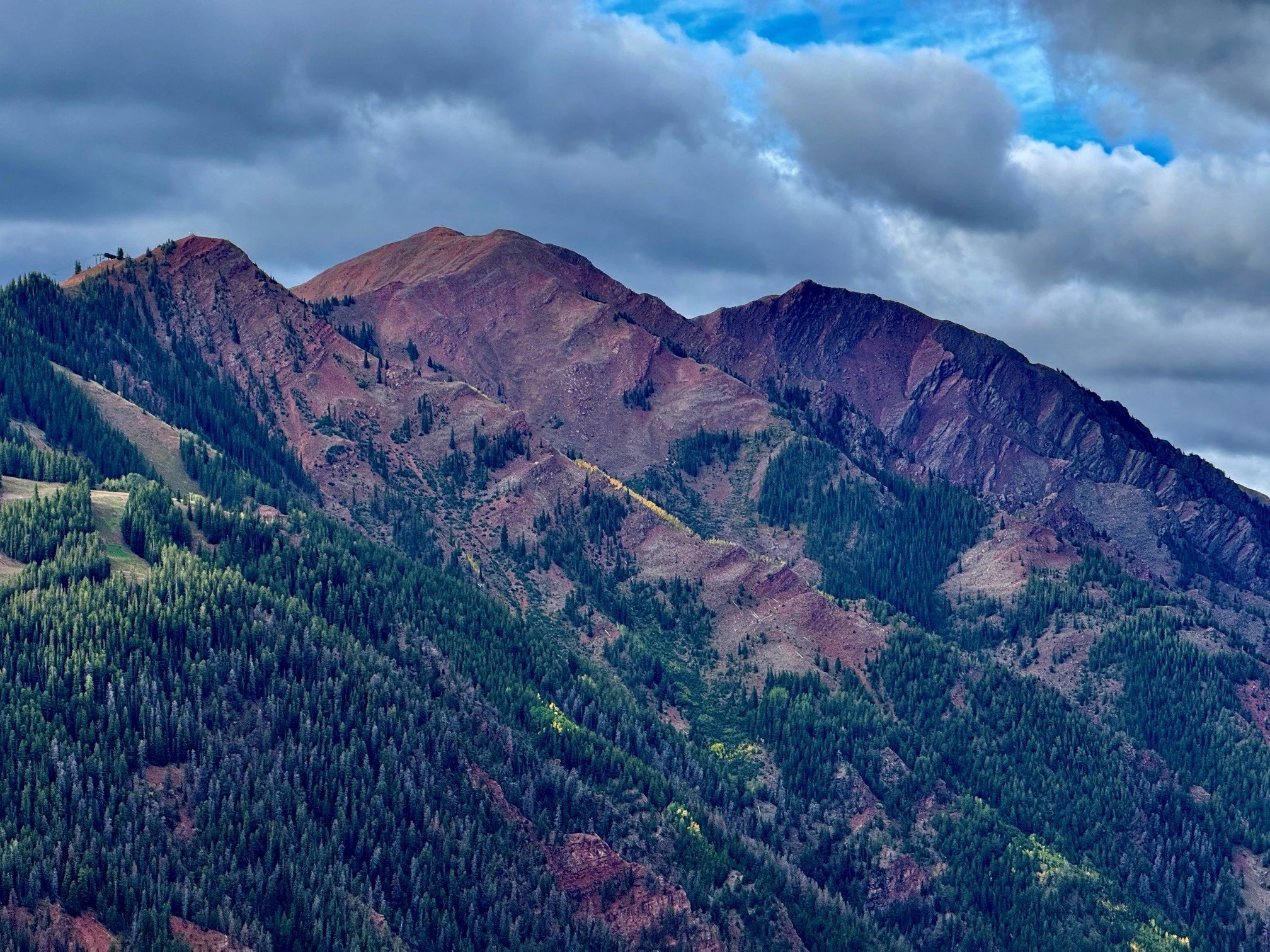 Rugged Aspen-area mountain ridges above a forest under dramatic clouds