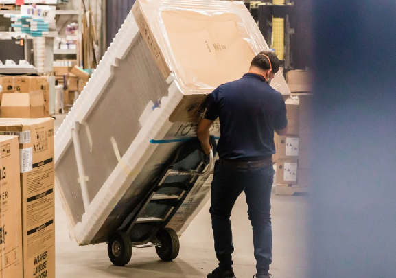 Worker using an appliance dolly to move a packaged appliance in a warehouse