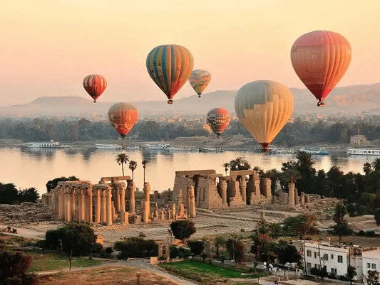 Hot-air balloons above Egyptian temples and the Nile in warm morning light