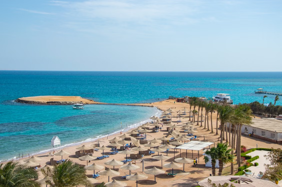 A palm-lined Hurghada beach with parasols beside the turquoise Red Sea