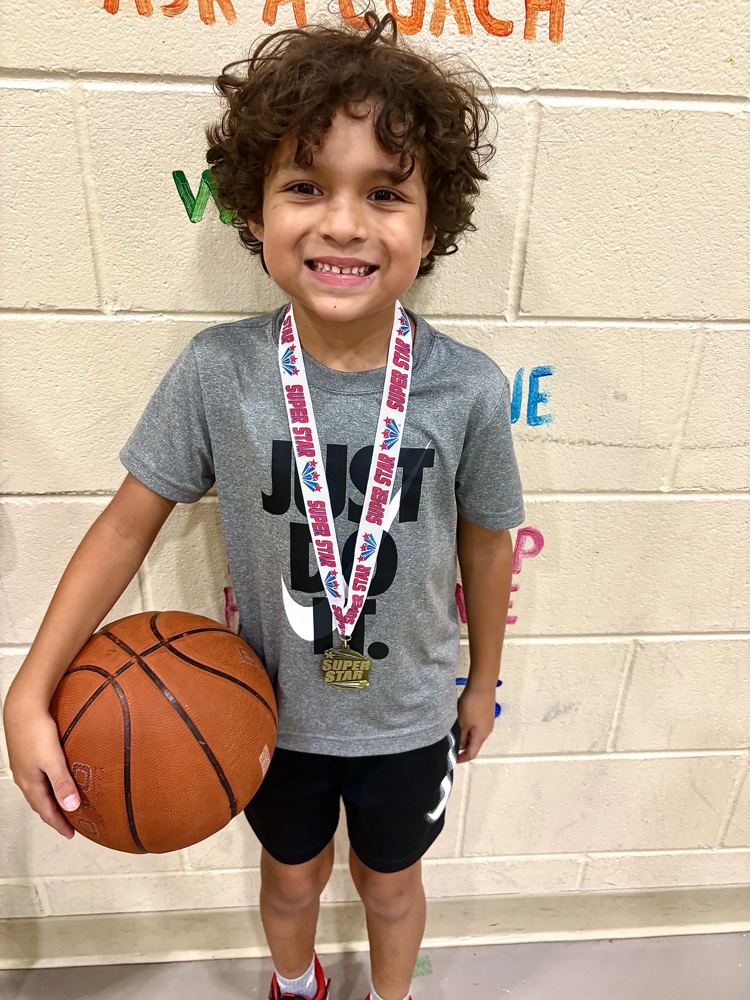 A smiling Texas SuperStars participant holding a basketball and wearing his medal