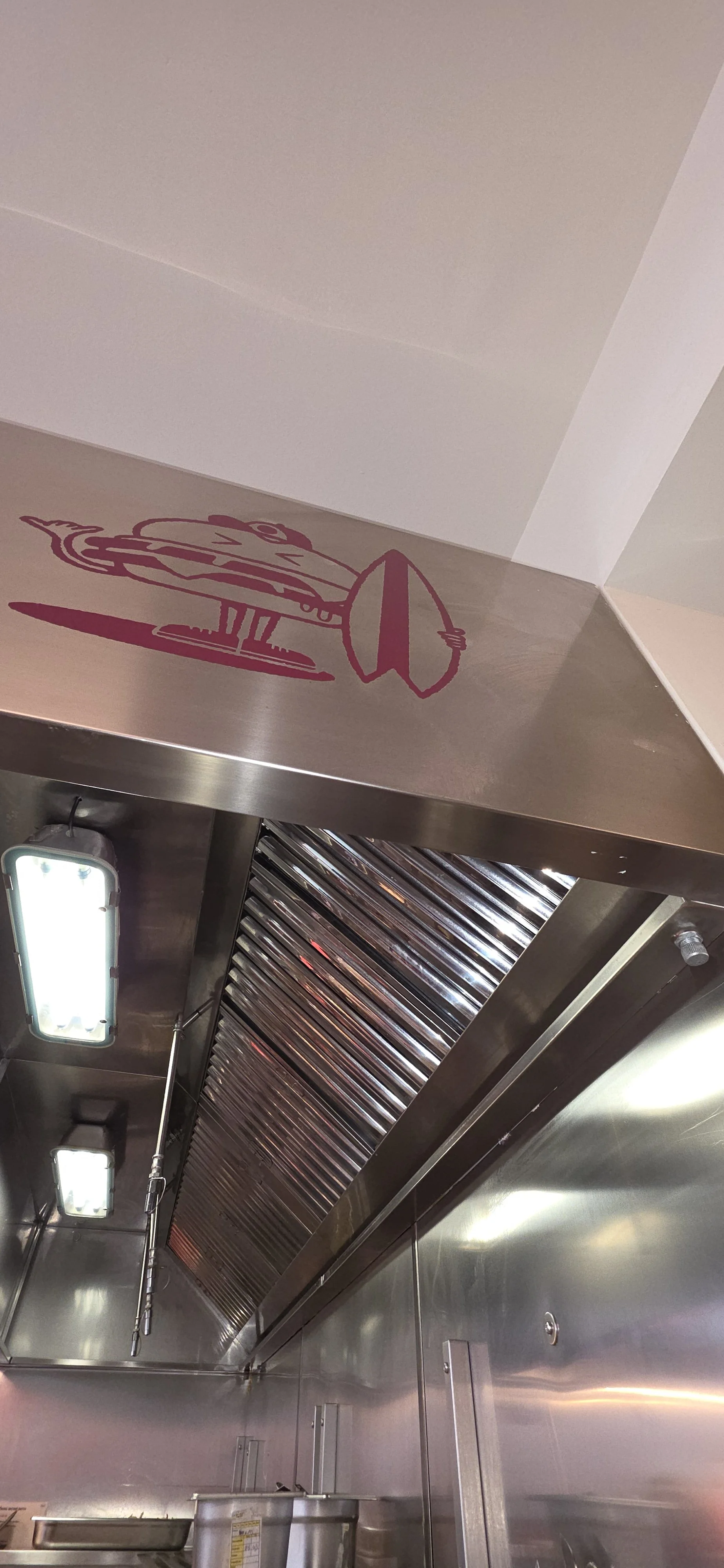 Hotte em inox com filtros metálicos e iluminação numa cozinha profissional