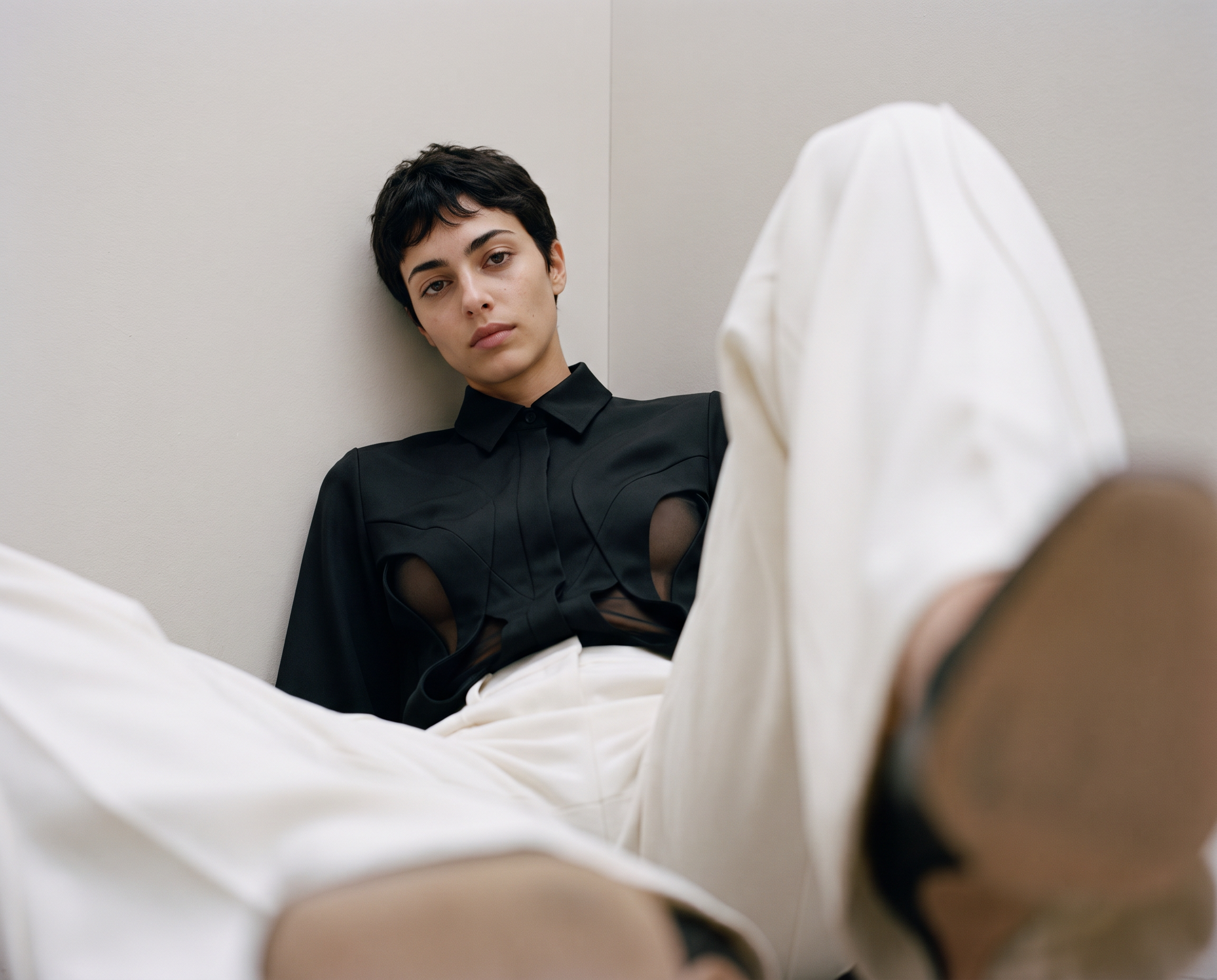 Model wearing the black Reliquary Blouse with curved sheer panels and ivory trousers