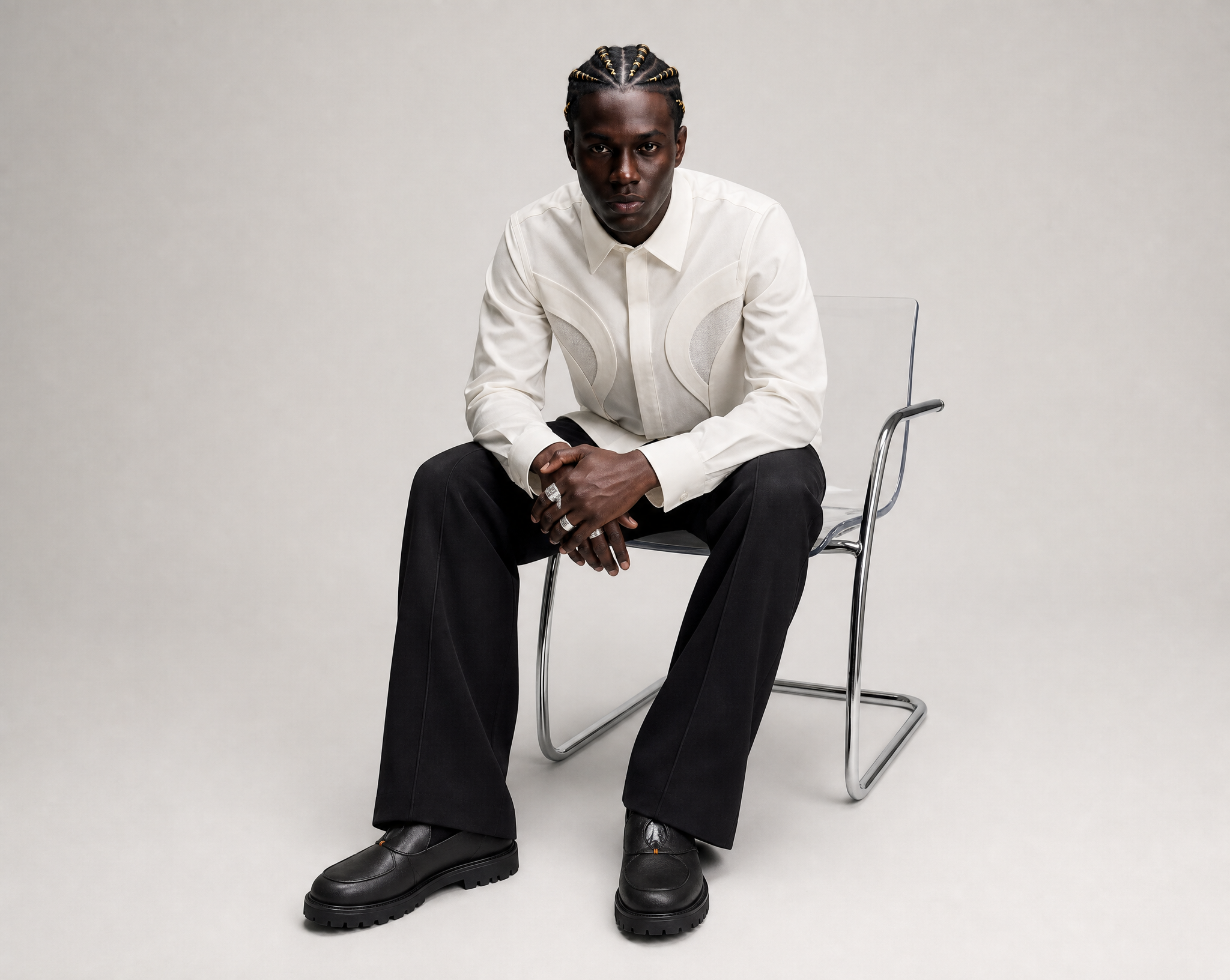 Seated model wearing the ivory Origin Shirt with curved sheer panels, black trousers and loafers