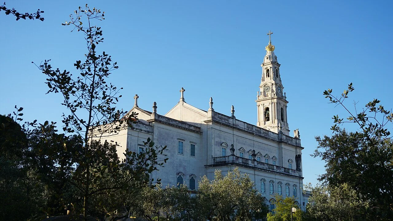 Basilica of Our Lady of the Rosary at Fátima, seen through trees beneath a blue sky.