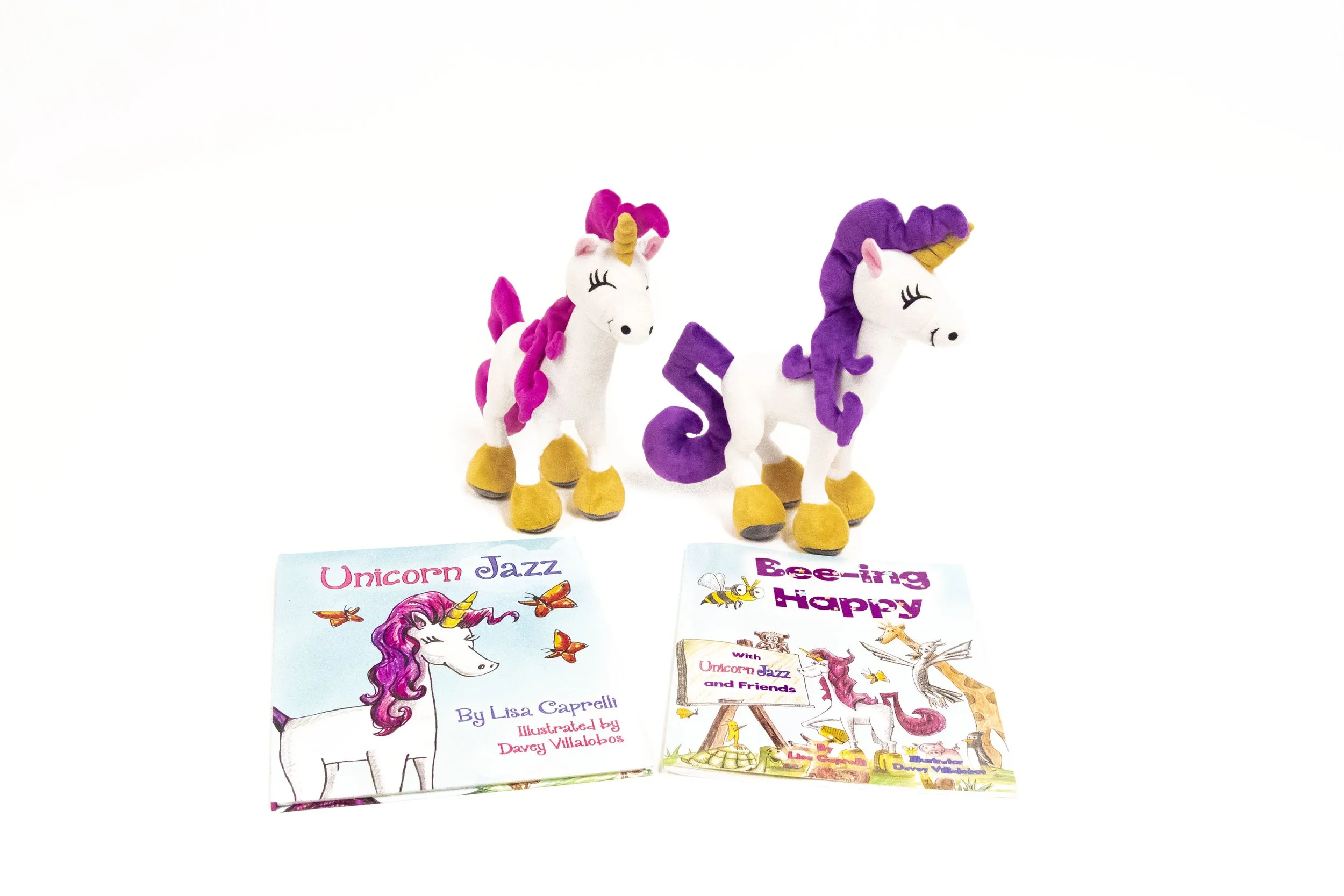 Pink- and purple-maned unicorn plush characters displayed with Unicorn Jazz and Bee-ing Happy books.