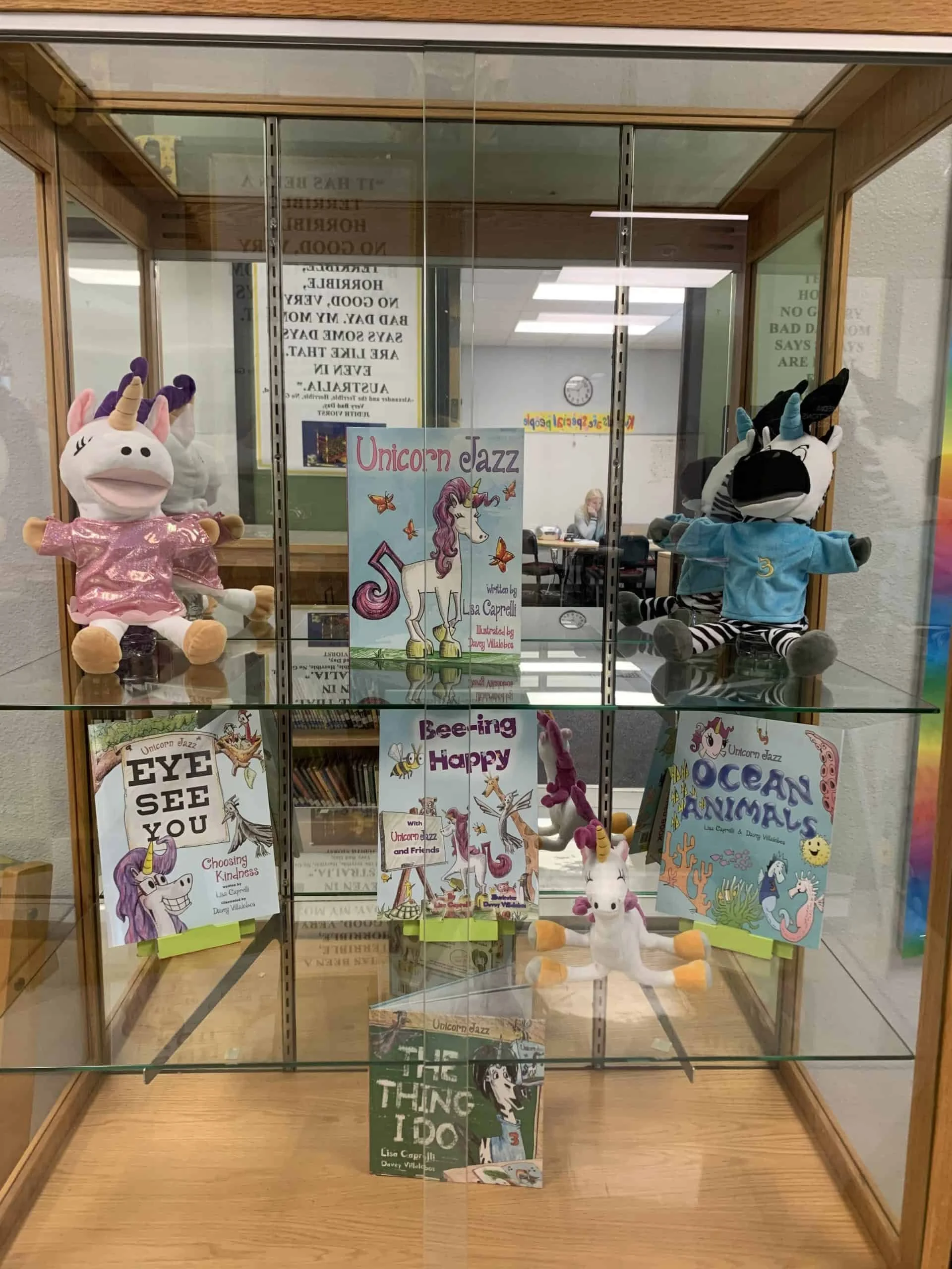 Unicorn Jazz books and puppets arranged inside a glass display case.