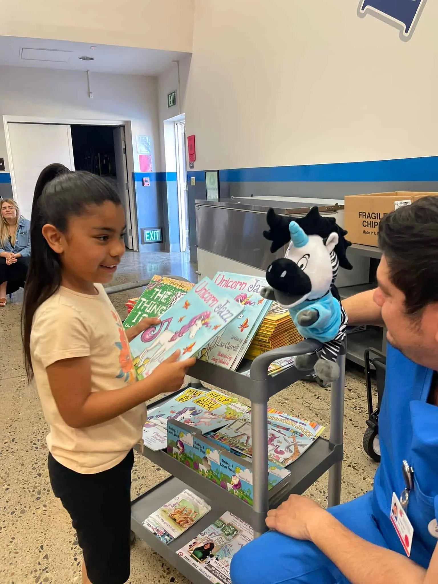 A child holding a Unicorn Jazz book beside an adult with a zebra puppet.