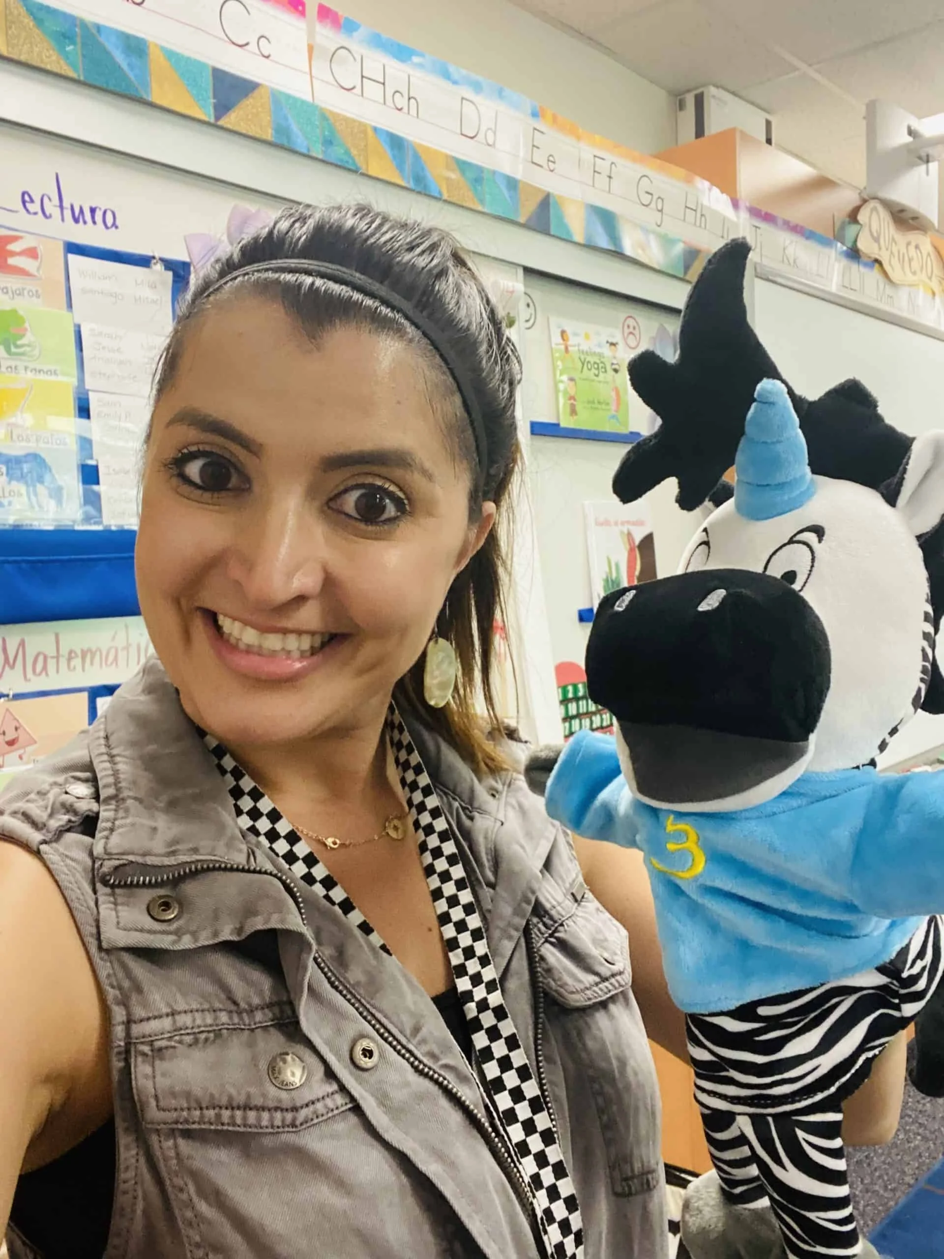 Woman beside a zebra puppet wearing a blue shirt in a classroom.