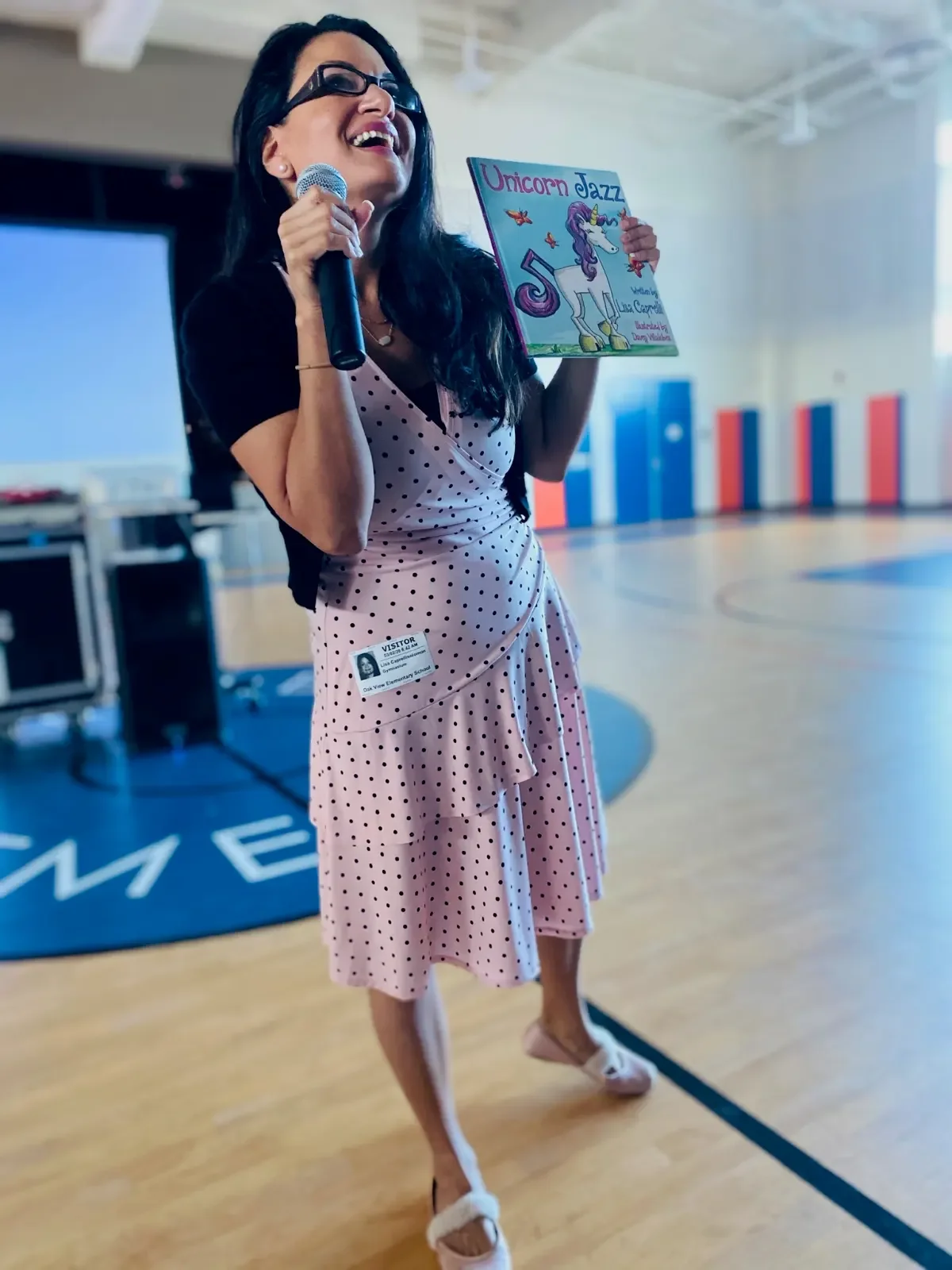 Lisa Caprelli speaking to students with a microphone and Unicorn Jazz book