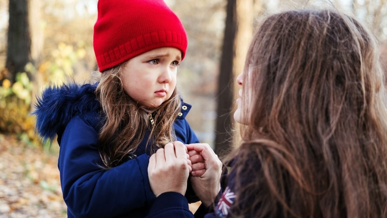 A child in a red hat talks with another person outdoors.