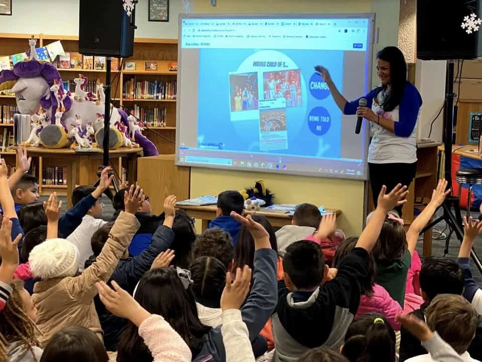 Lisa Caprelli speaks to children raising their hands during a school presentation.