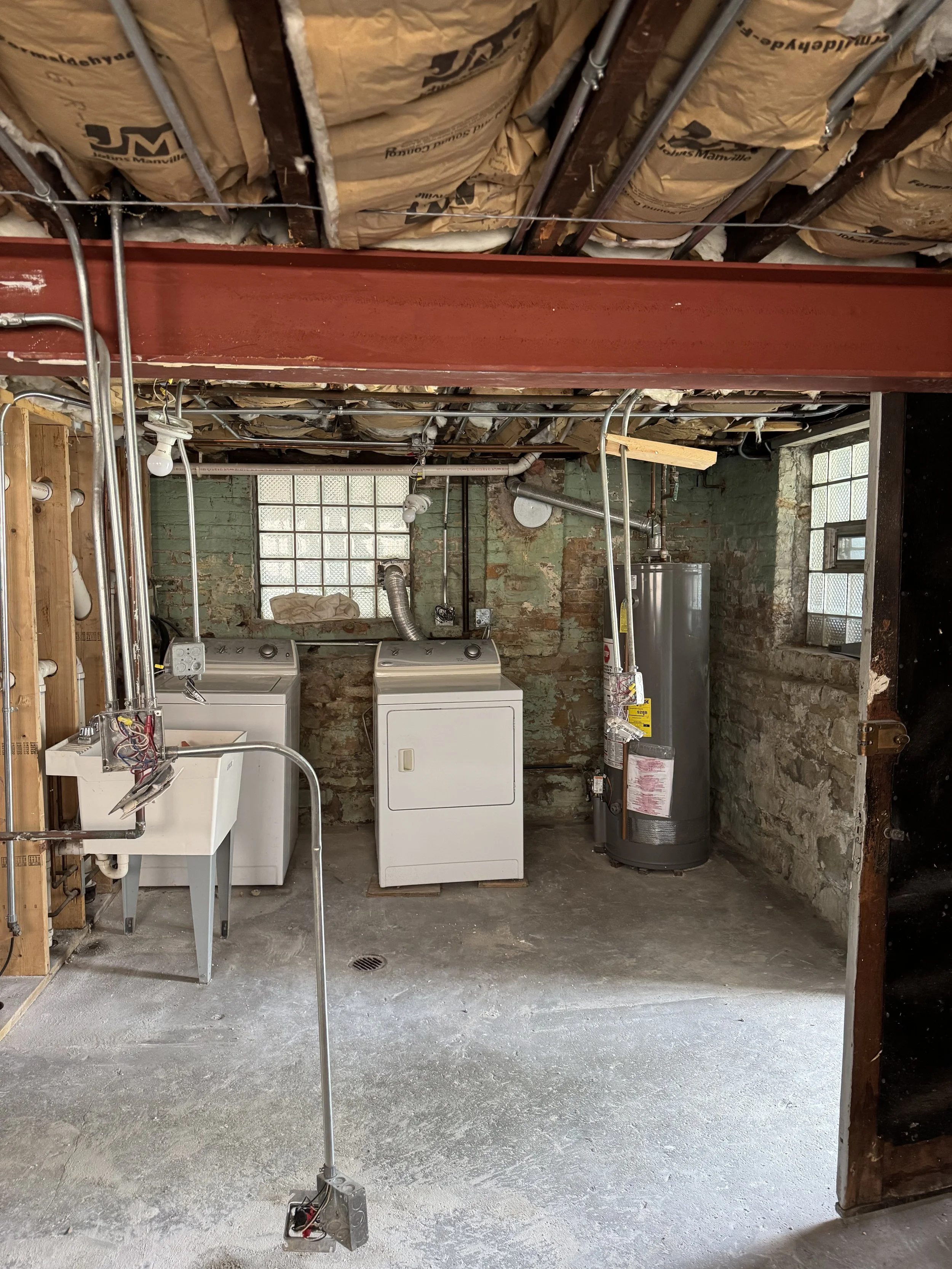 The laundry area with washer, dryer and water heater against a painted brick wall