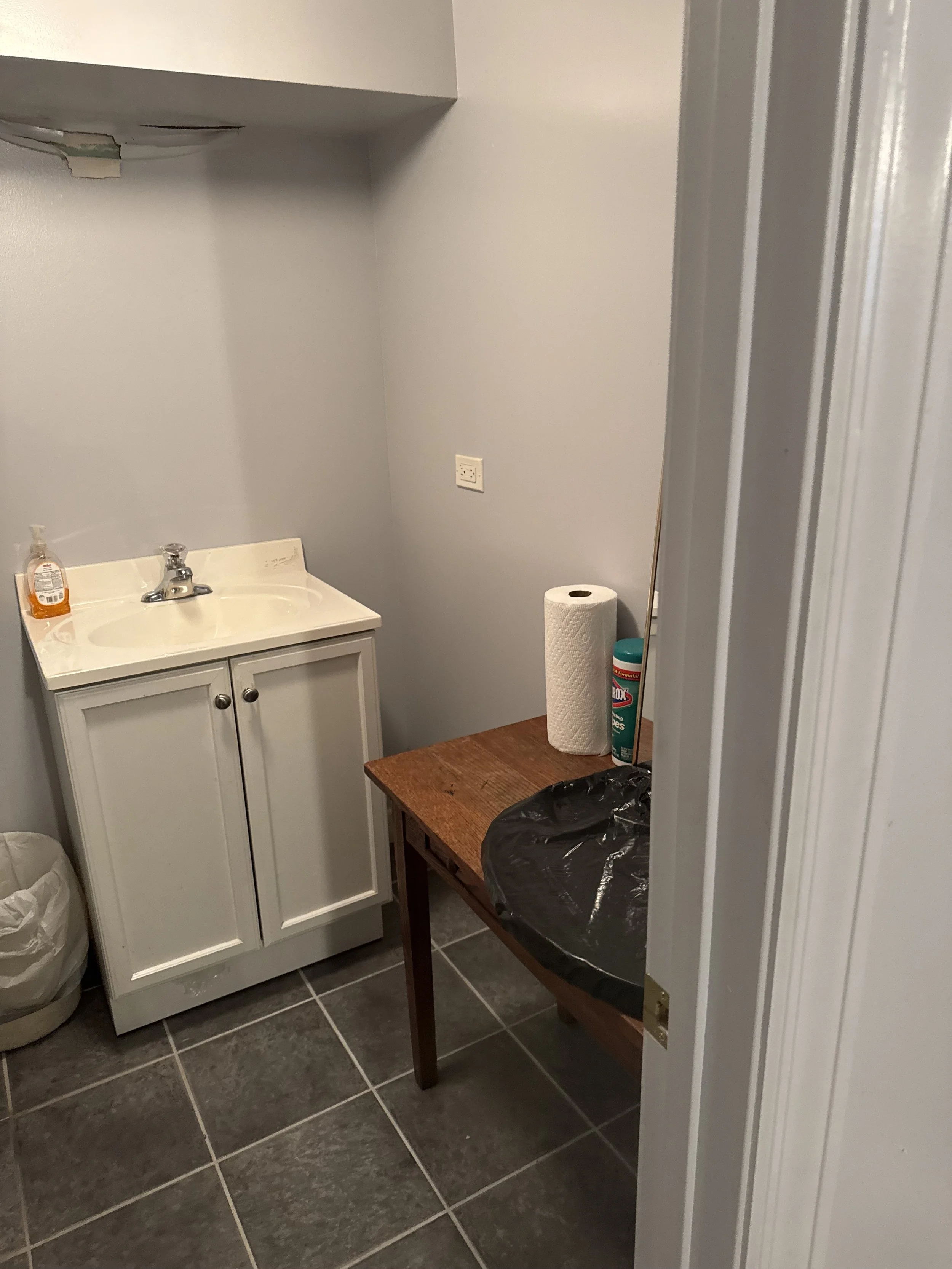The old basement bathroom with a white vanity and grey tile floor