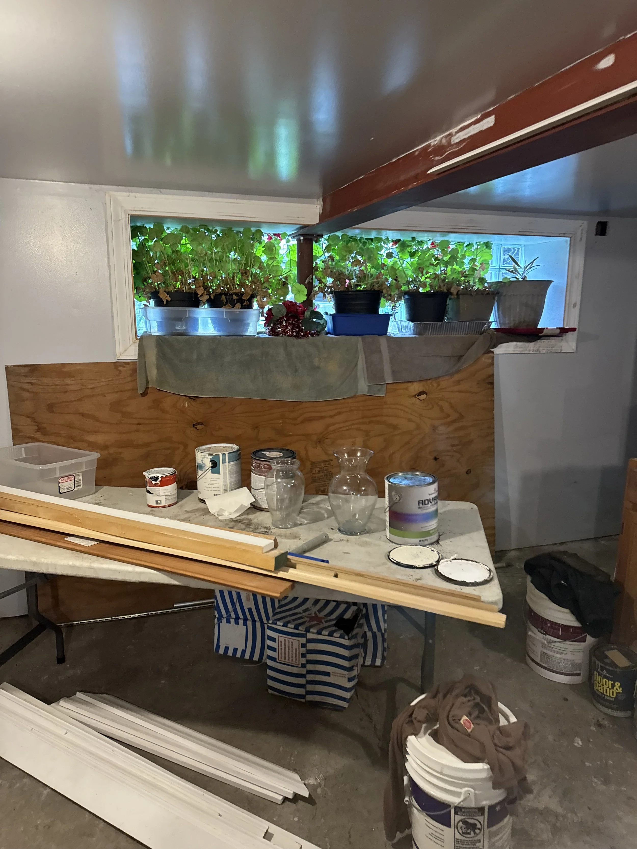 A basement work area with paint cans and a window at ground level