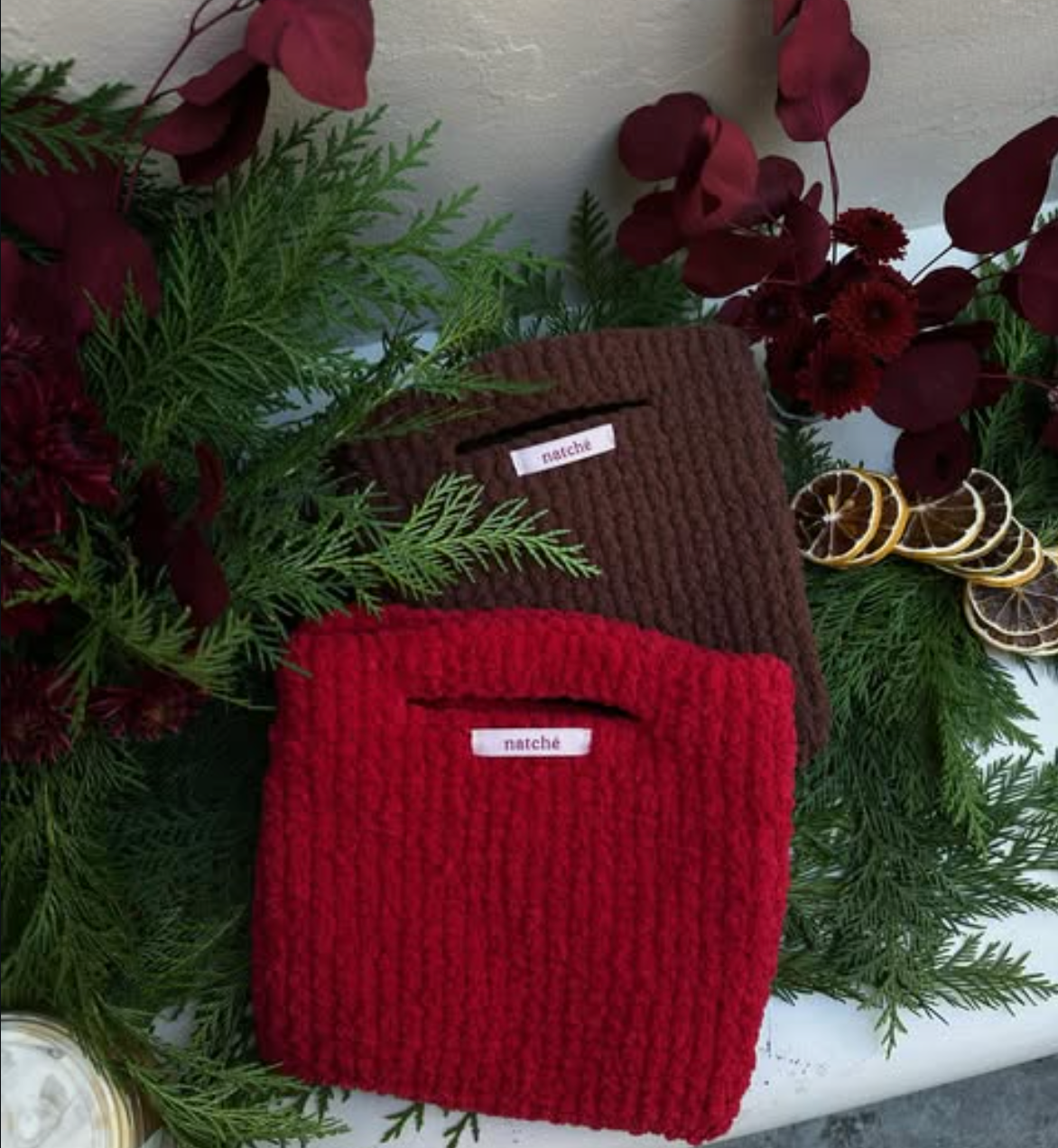 Knitwear displayed with burgundy florals and evergreen foliage