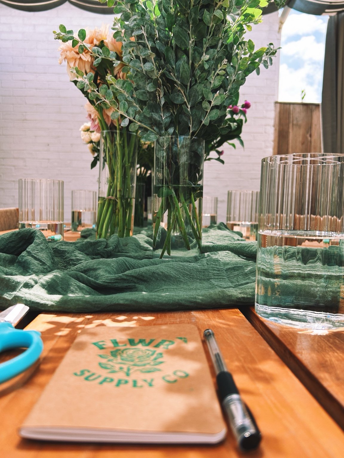 FLWR notebook, glassware and flowers on a workshop table