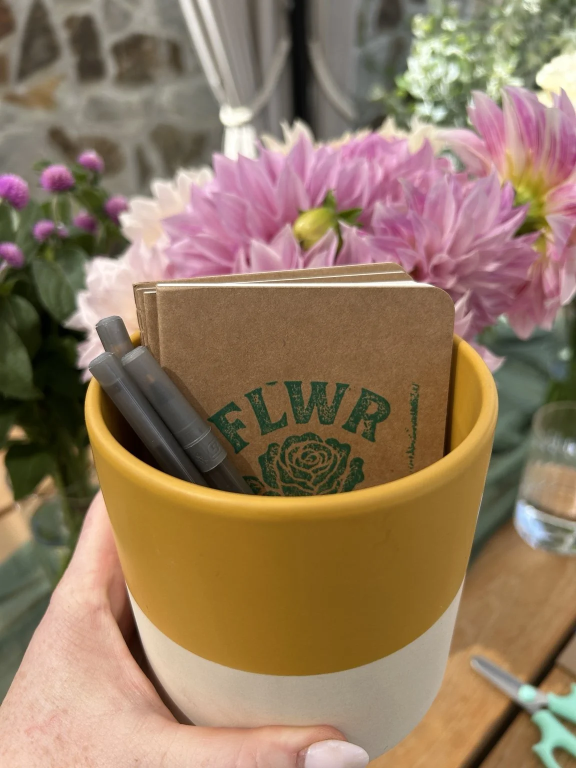 FLWR notebook and pens in a yellow ceramic cup