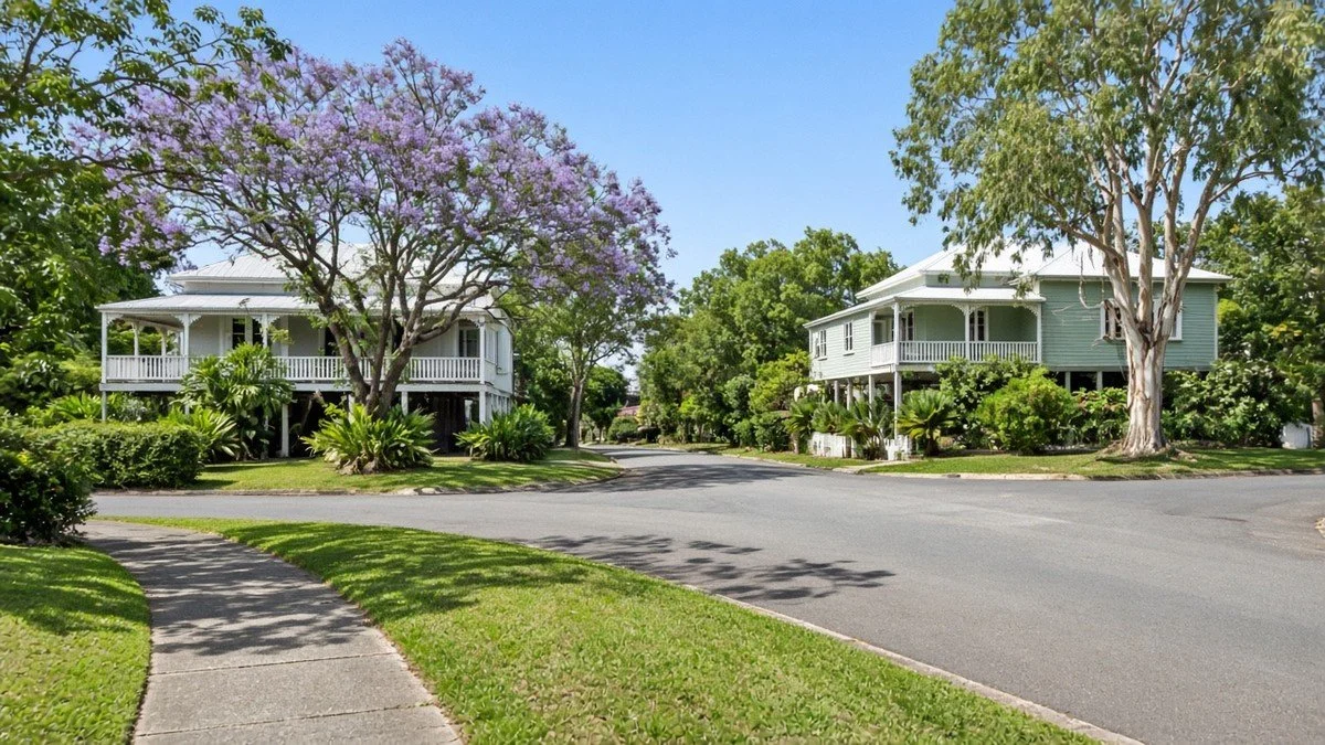Leafy Brisbane street intersection with Queenslander homes and a flowering jacaranda