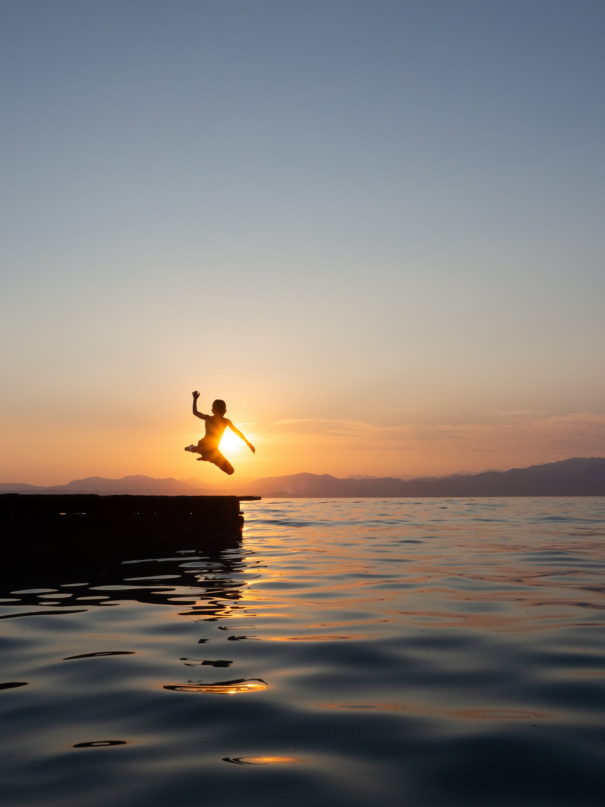 A child leaping from a dock into a lake at sunset