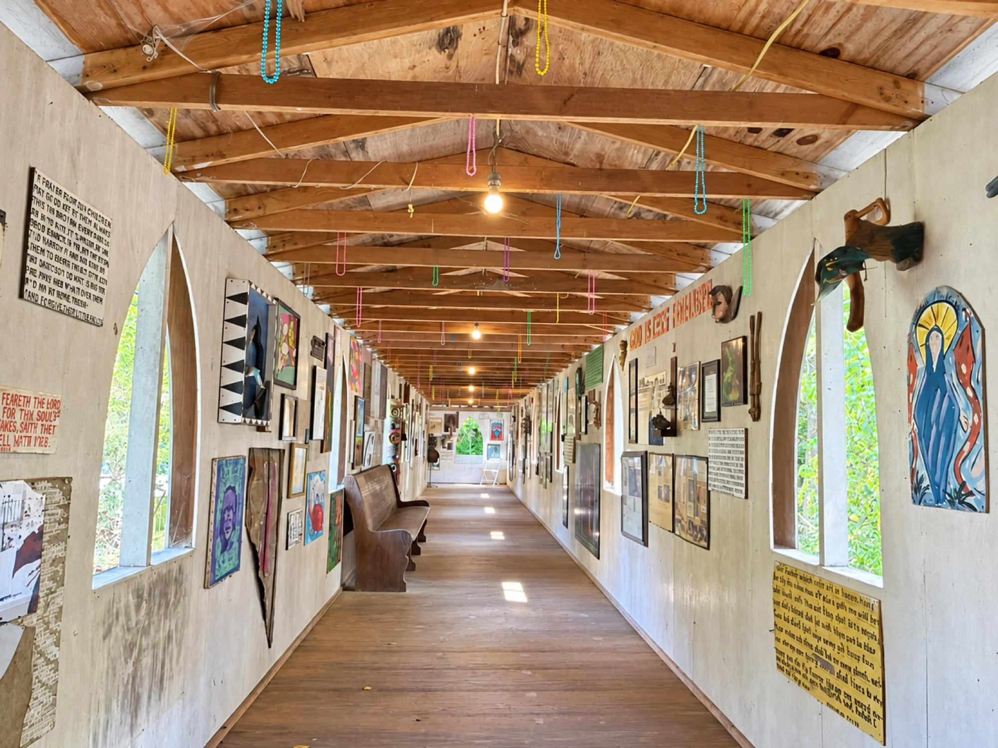 A long gallery corridor at Paradise Garden lined with artwork, scripture, objects, and arched window openings
