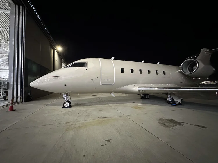 Large-cabin jet on the ramp outside a lit hangar at night
