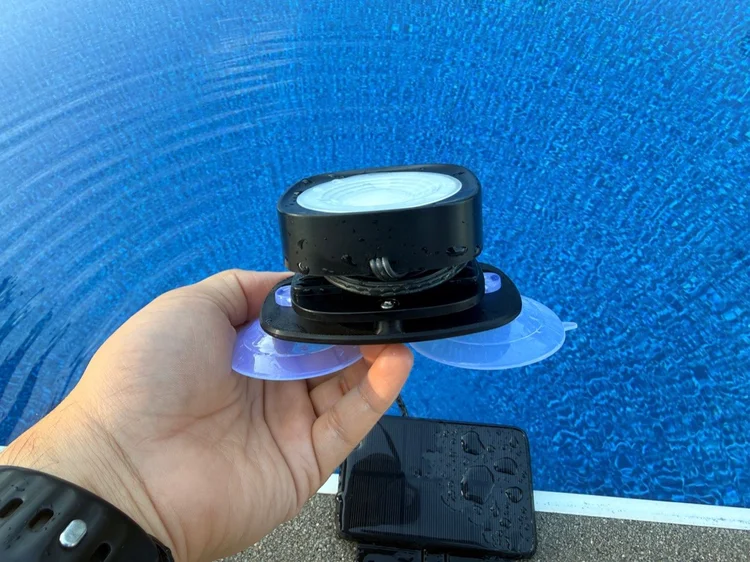 Pool light attached to a custom black bracket with two large suction cups, held beside a pool.