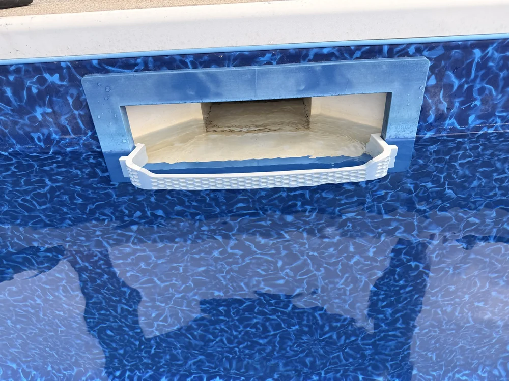 Protector blanco personalizado con patrón de panal instalado frente a la abertura del skimmer de pared de una piscina.