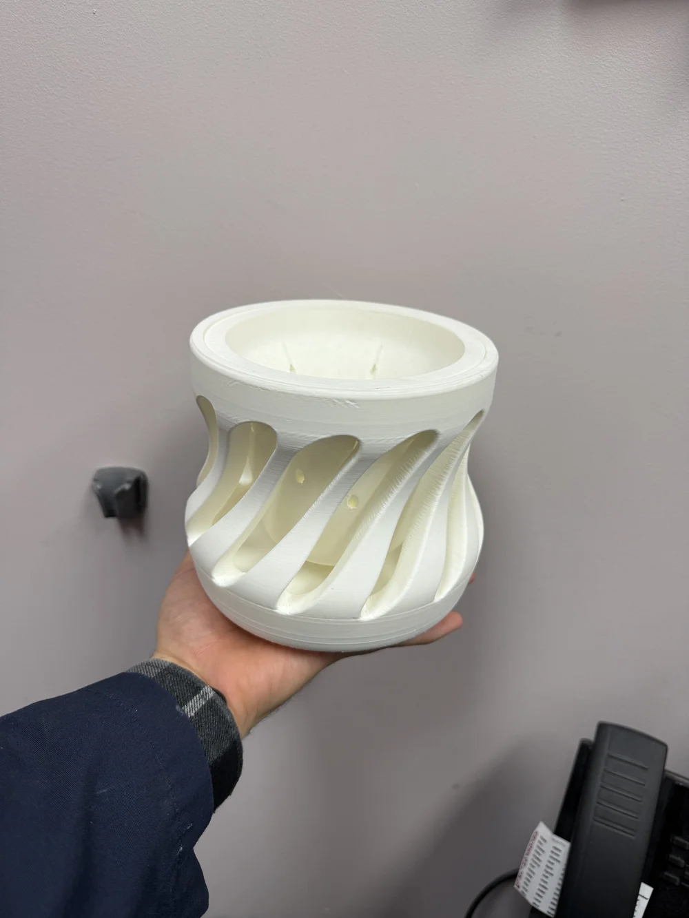 Maceta blanca de forma escultórica con aberturas curvas, sostenida con una mano para mostrar su tamaño.