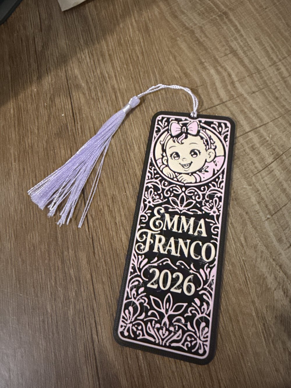 Separador de libros decorativo rosa y negro para baby shower, con borla lila sobre una superficie de madera.