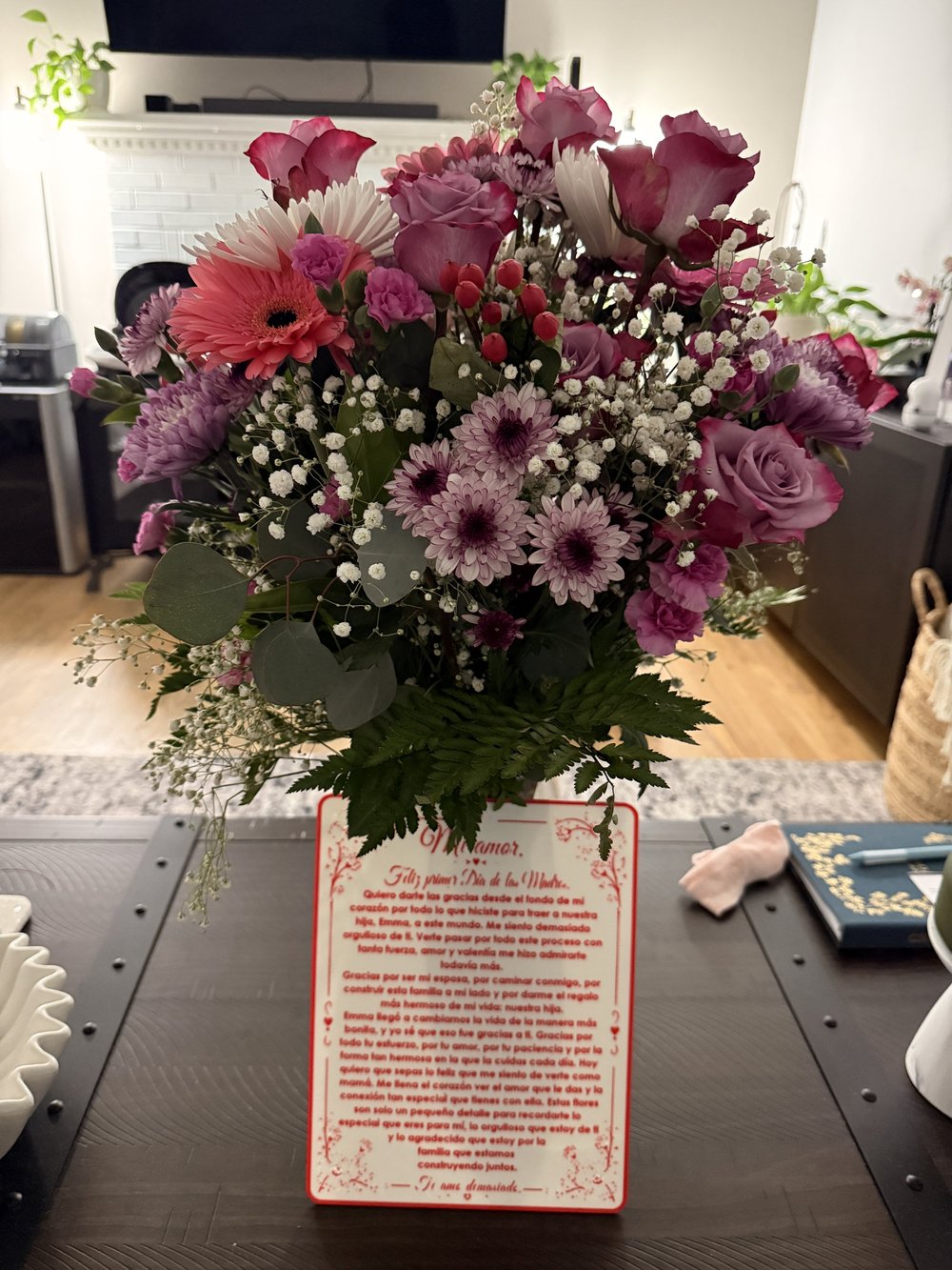 Tarjeta blanca y roja personalizada para el Día de las Madres, colocada debajo de un arreglo floral.