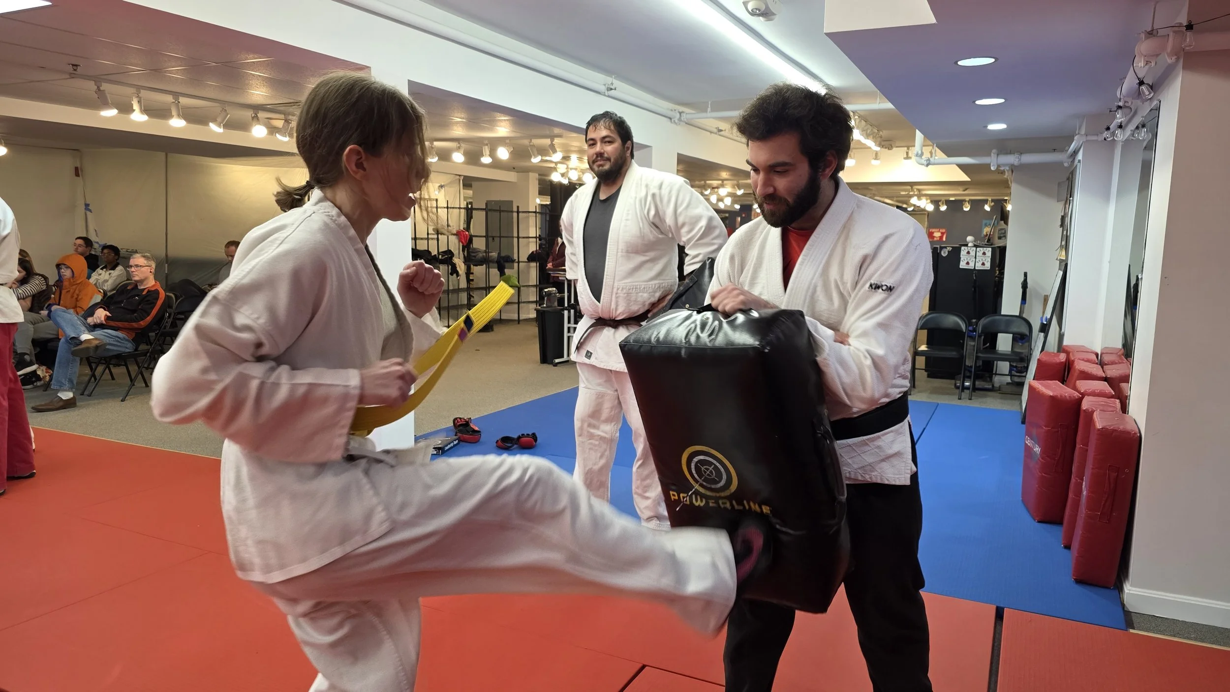 A student practicing a kick against a pad held by a training partner