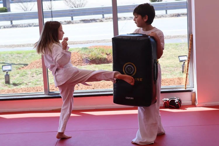 A Little Ninjas student practicing a kick with a coach and training pad