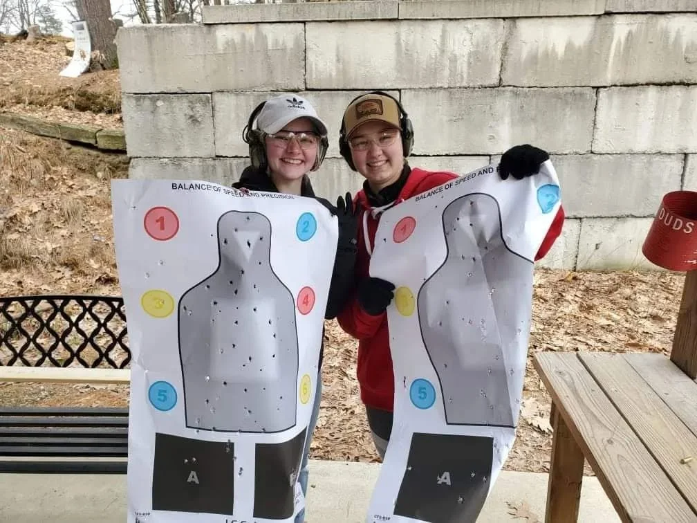 Two range participants wearing hearing protection and holding paper targets
