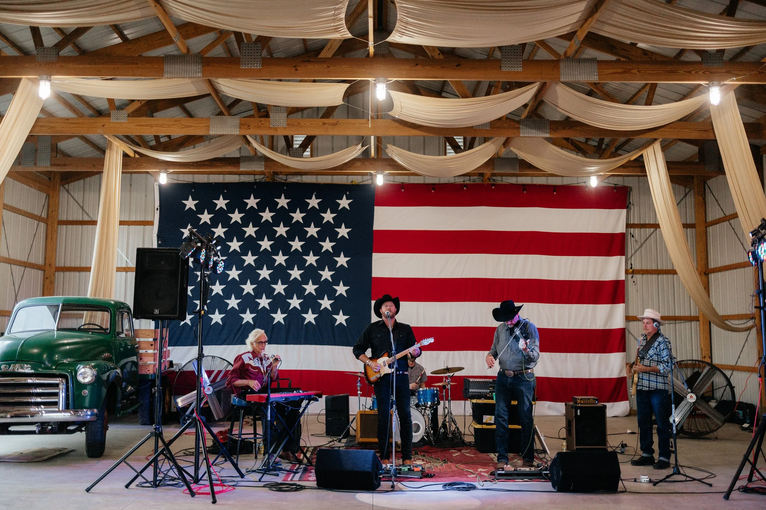 Musicians playing in the barn beside a vintage green truck