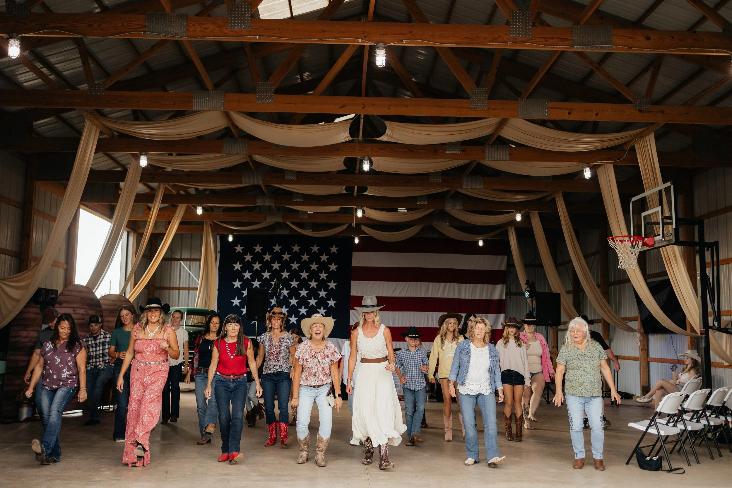 Guests line dancing in the Gathering Barn beneath draped fabric and an American flag