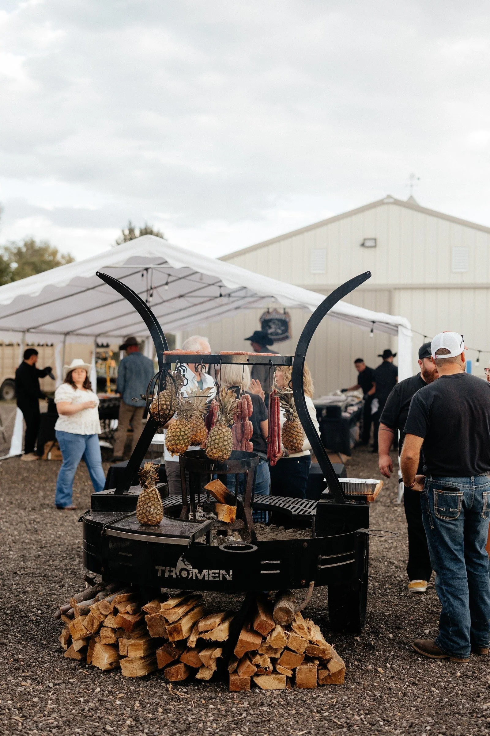 Wood-fired grill with hanging food and stacked firewood at Legacy Family Night